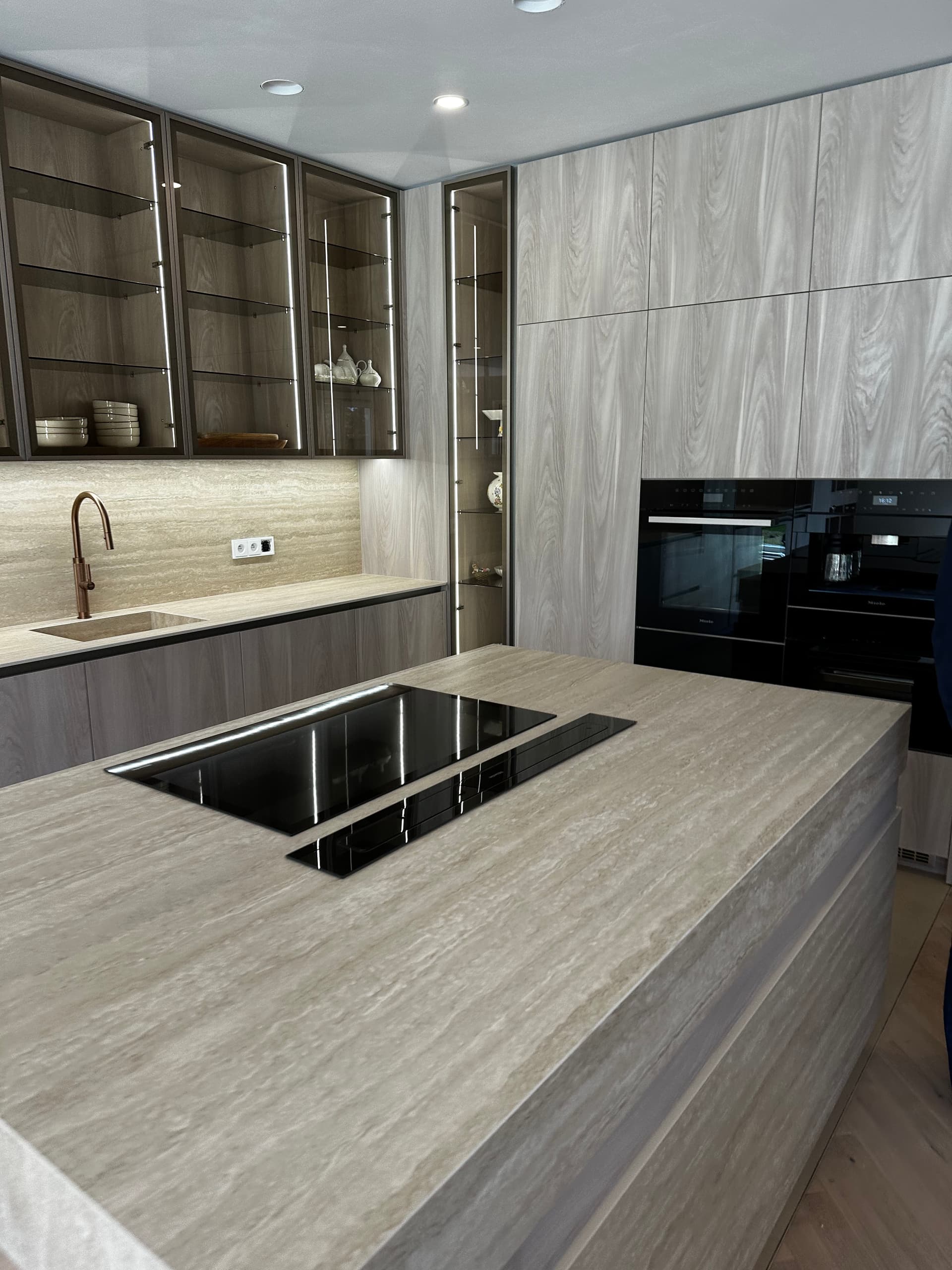 Glass-front cabinets with integrated LED lighting and travertine backsplash